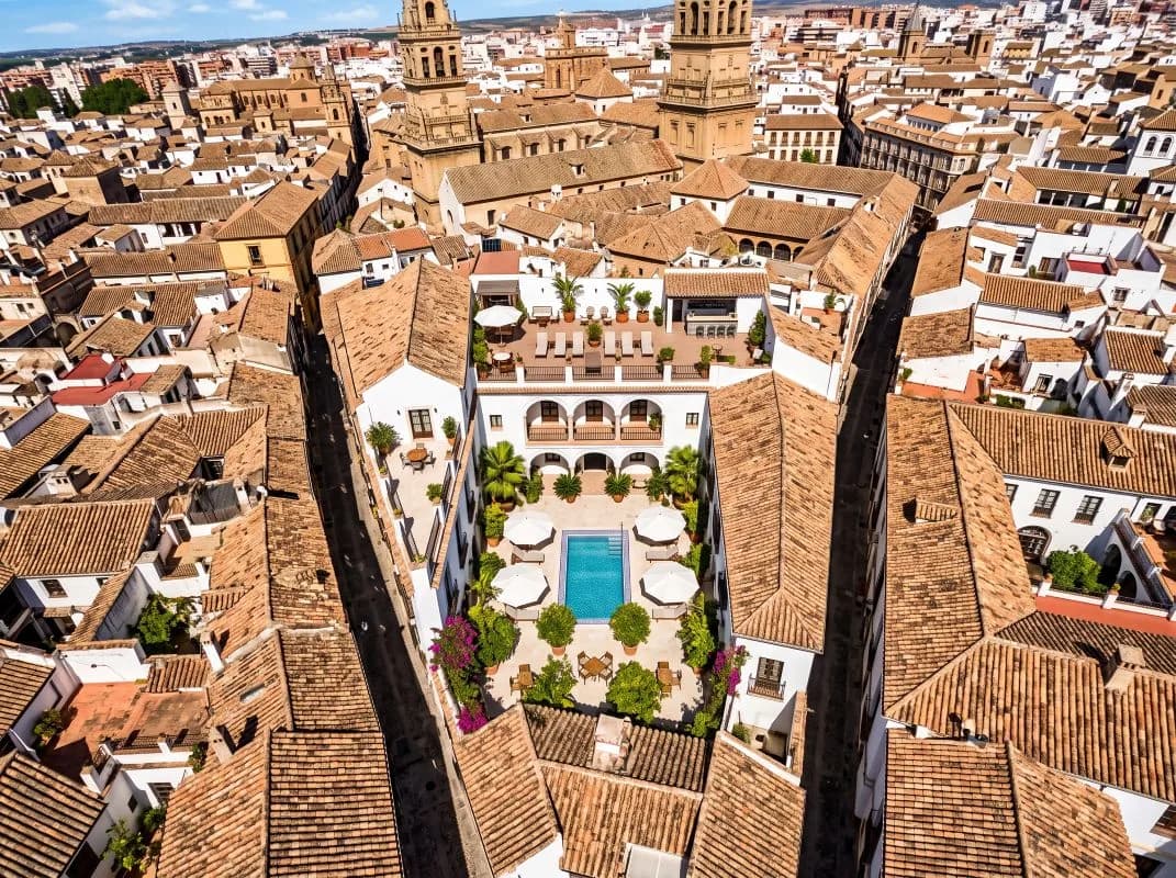 Vista aérea de un hotel con patio y piscina entre los tejados del casco histórico de una ciudad